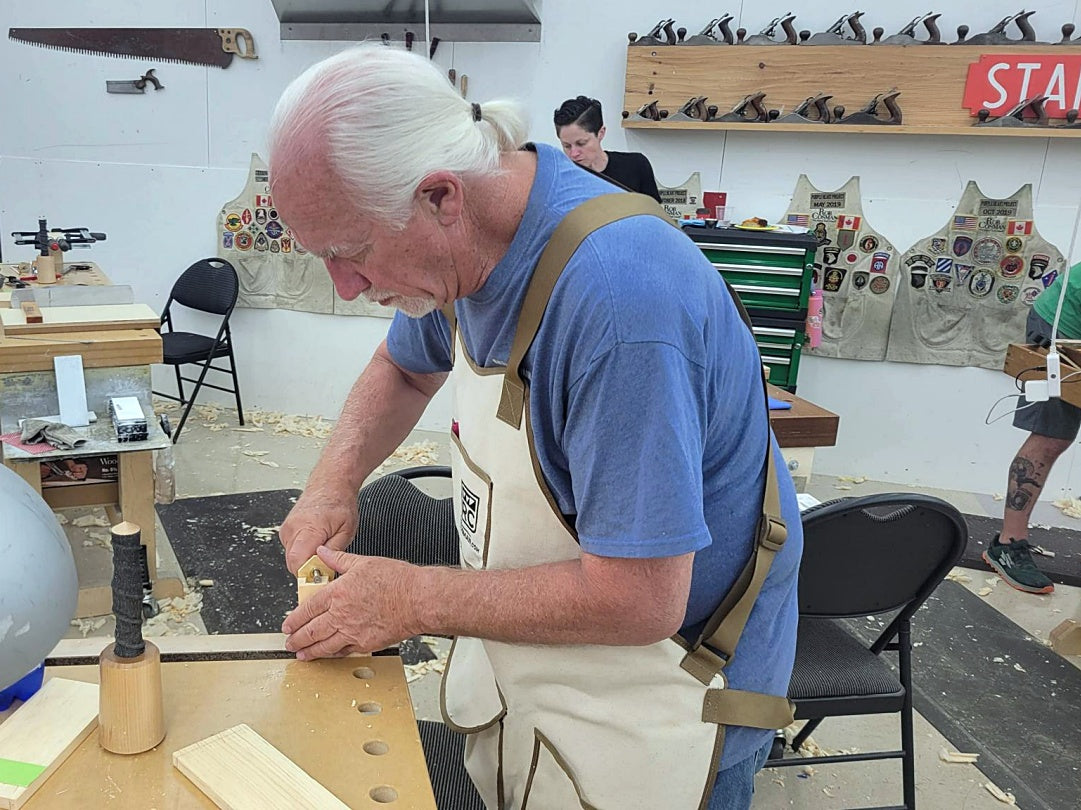Man working on a wooden project in a workshop with various tools and equipment around.