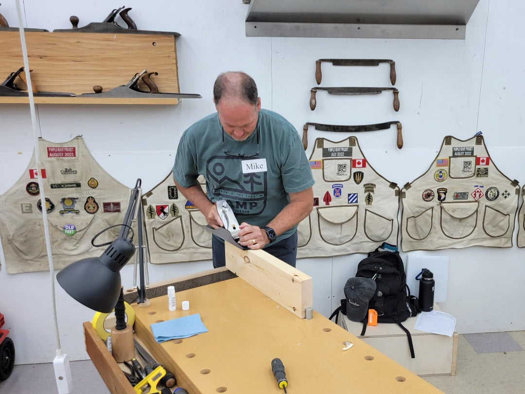 Man working at a wooden workbench with tools and aprons in the background