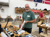 Man in a workshop holding a tool, with various tools and equipment around him.