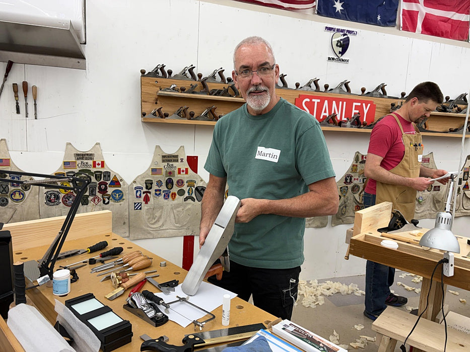 Man in a workshop holding a tool, with various tools and equipment around him.