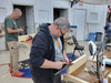 Two men working on a project in a workshop with tools and materials around.