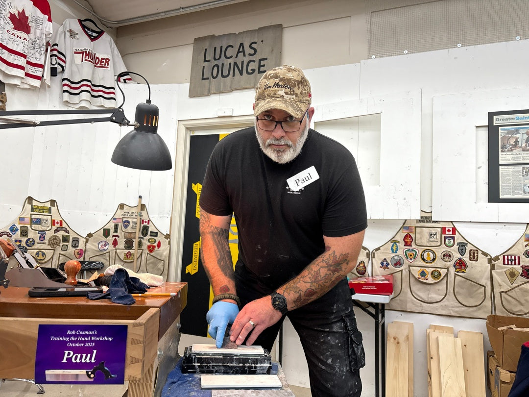 Man in a workshop setting with various items and a sign reading 'Lucas' Lounge'.