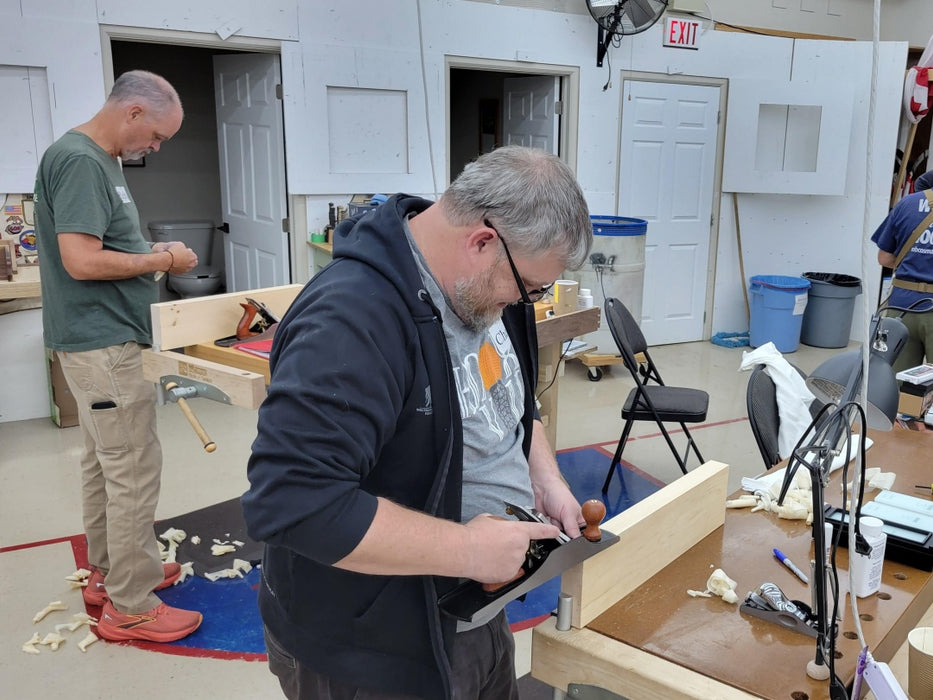 Two men working on a project in a workshop with tools and materials around.