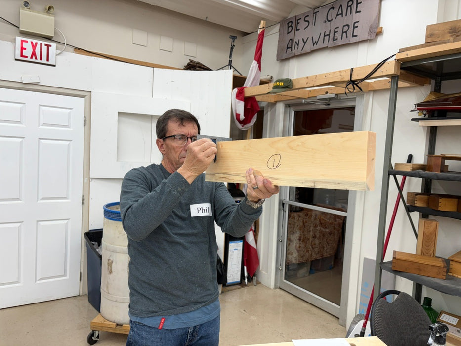 Man holding a wooden board in a workshop with 'Best Care Anywhere' sign in the background