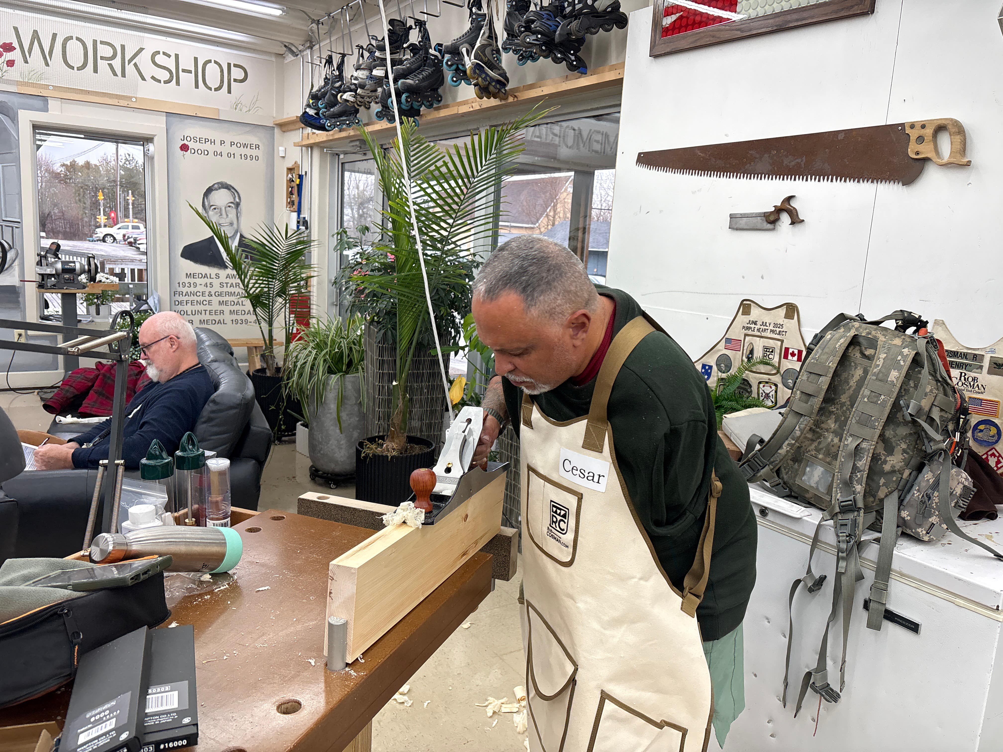 Man in a workshop wearing an apron, surrounded by tools and equipment.