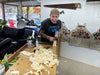 Man working with wood in a workshop with various tools and equipment around.