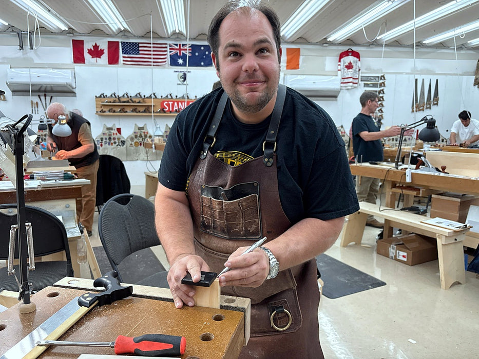 Man in a workshop wearing an apron, holding a tool.
