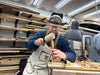Man in a workshop using a hammer and chisel, wearing a protective helmet and apron.