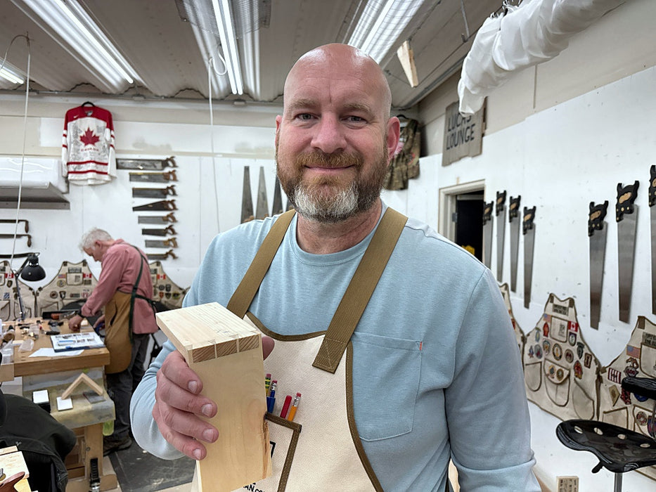 Man in a workshop holding a wooden block, with tools and equipment in the background.