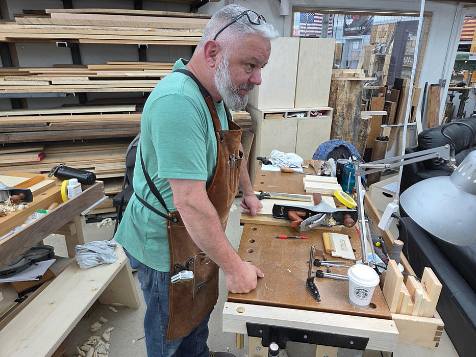Man working in a woodworking shop with tools and wood pieces around.