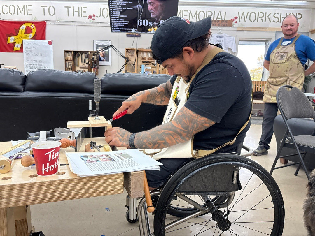 Person in a wheelchair working on a project at a table with various items, including a TV screen in the background.