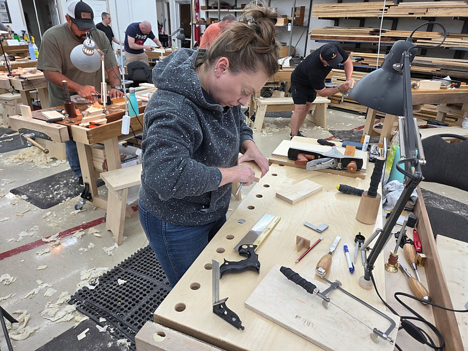 Person working on a wooden surface with tools and materials in a workshop setting.