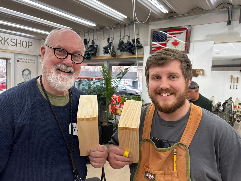 Two men holding wooden dovetails in a workshop setting.