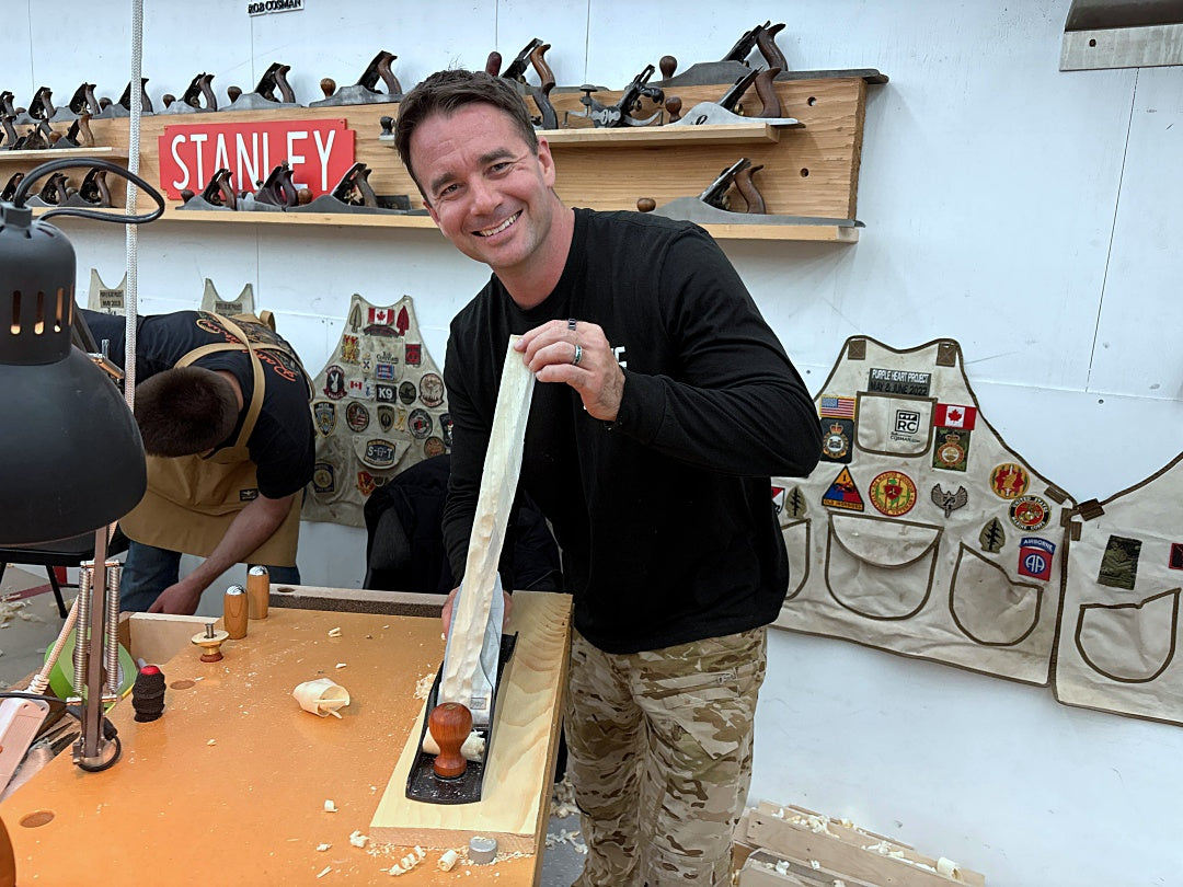 Man in workshop holding a piece of wood, with tools and Stanley branding in the background.