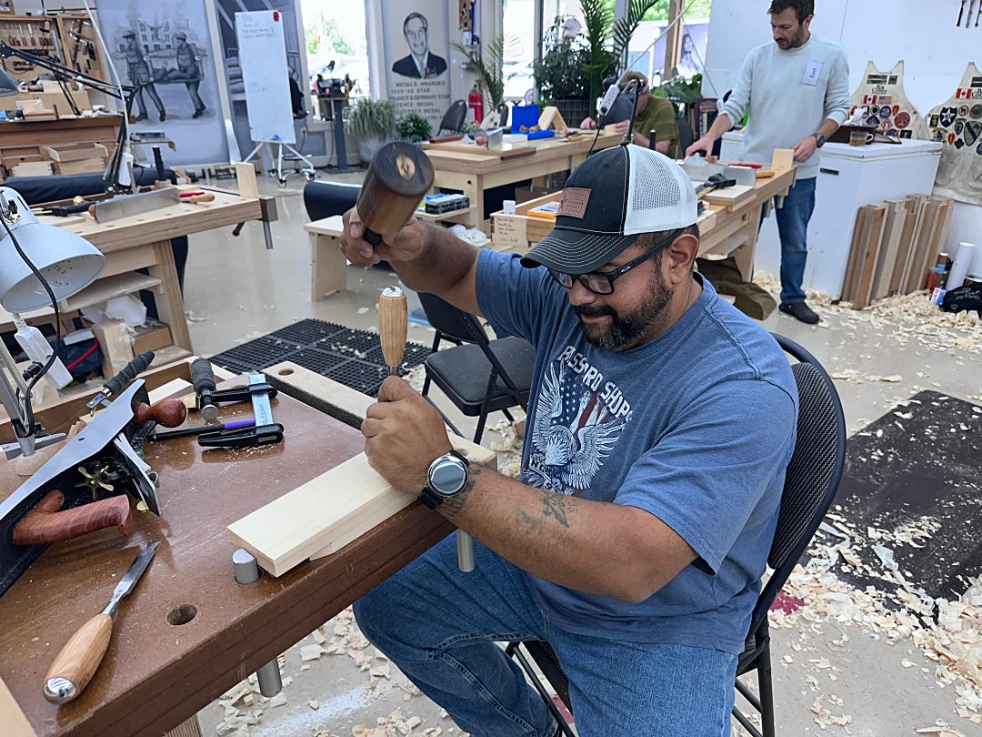 Man working on a wooden project in a workshop with tools and materials around.