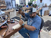 Man working on a wooden project in a workshop with tools and materials around.
