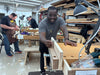 Man working with wood in a workshop with tools and materials around.