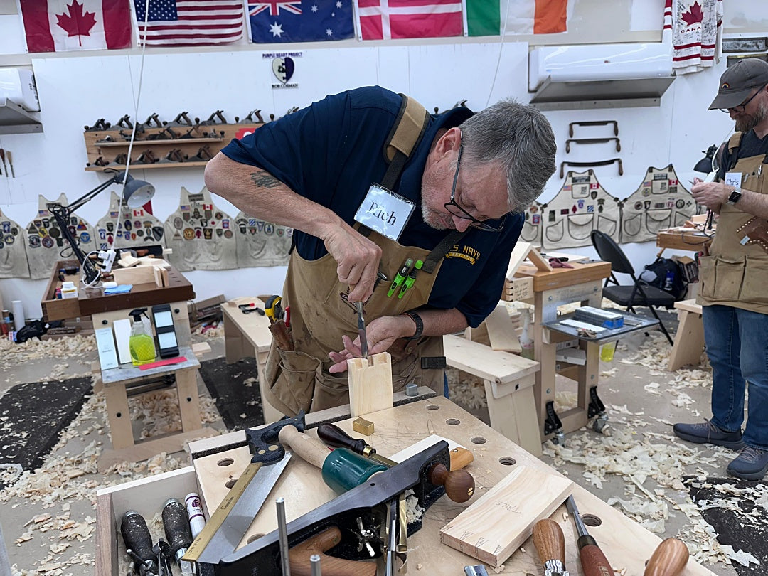 Man working on a wooden project in a workshop with various tools and wood pieces around.
