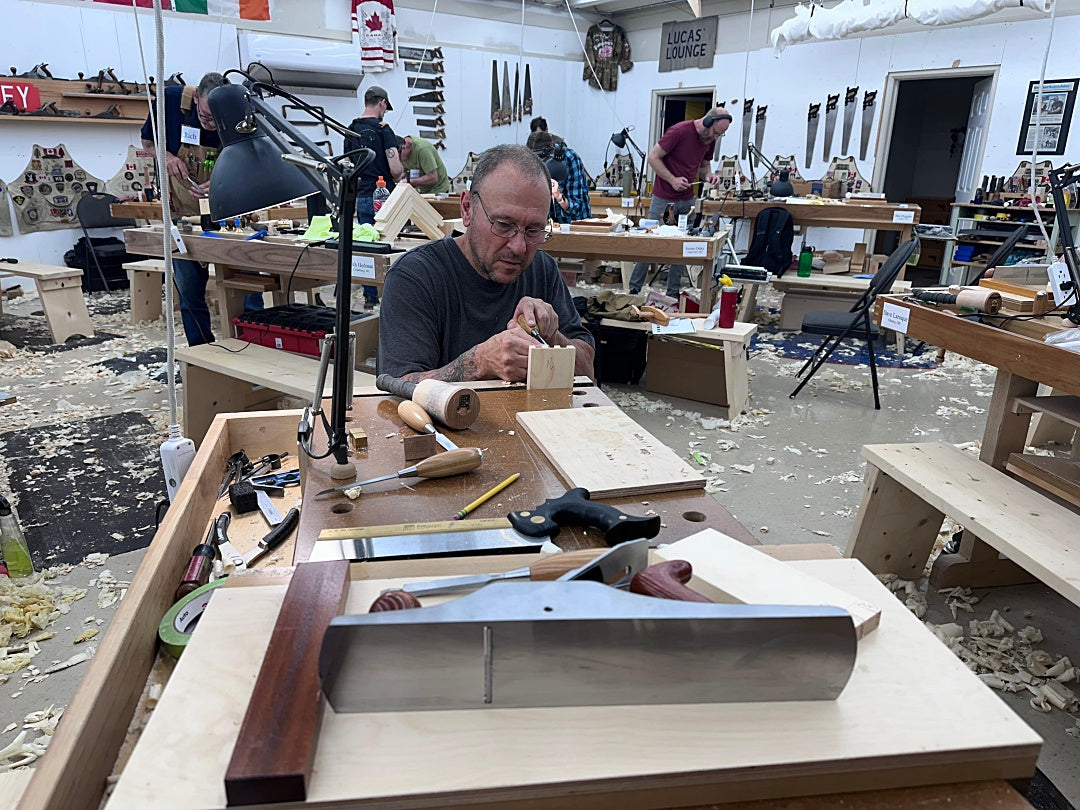 Man working on a wooden project in a workshop with various tools and materials around.
