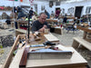 Man working on a wooden project in a workshop with various tools and materials around.