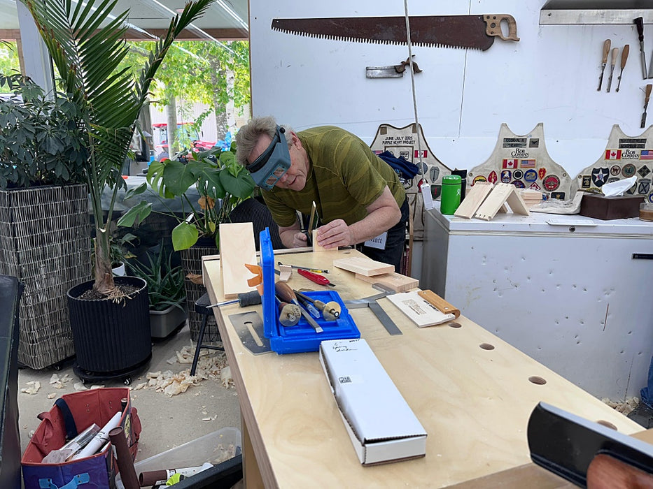 Person working at a wooden workbench with tools and materials in an outdoor setting