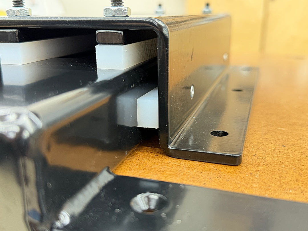 Close-up of a black metal mounting bracket or rail assembly with white rectangular inserts, photographed on a tan wood or cork surface.