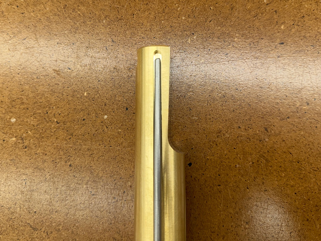 A close-up of a Rob Cosman 1-inch brass bench dog on a brown background.