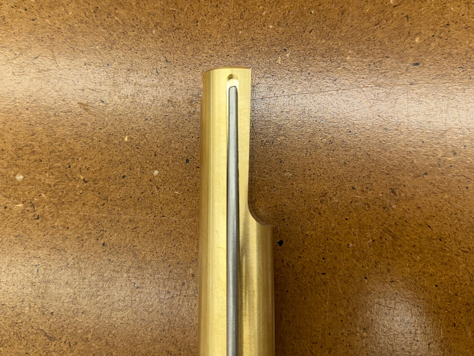 A close-up of a Rob Cosman 1-inch brass bench dog on a brown background.