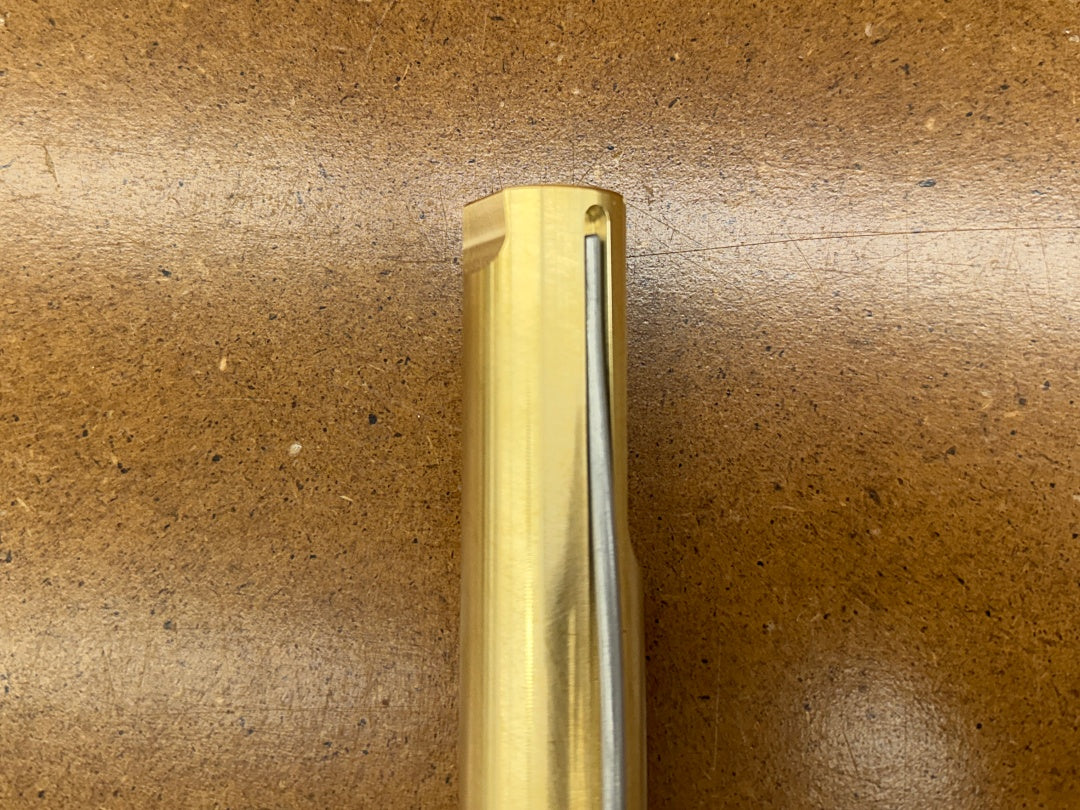 A close-up of a Rob Cosman 1-inch brass bench dog resting on a brown textured surface.
