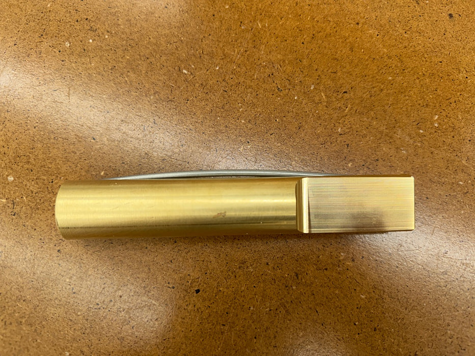 A rob cosman 1-inch brass bench dog  on a brown textured surface.