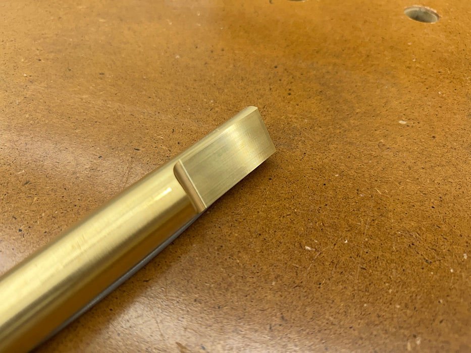 A close-up of a Rob Cosman 1-inch brass bench dog resting on a brown wood surface.