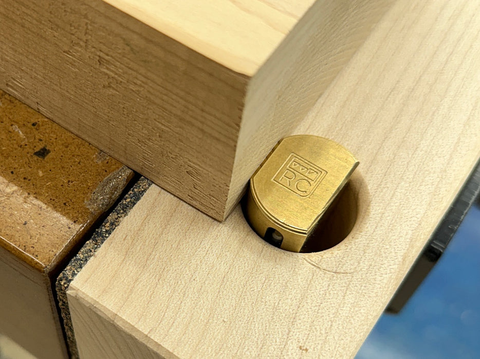 A close-up of a Rob Cosman 1-inch brass bench dog holding a piece of wood with its secondary faced