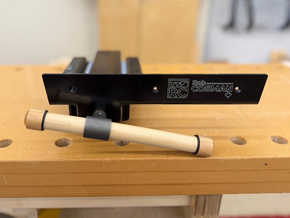 A close-up of a Rob Cosman Woodworking Vise, resting on a wooden workbench with a wooden-handle in front.