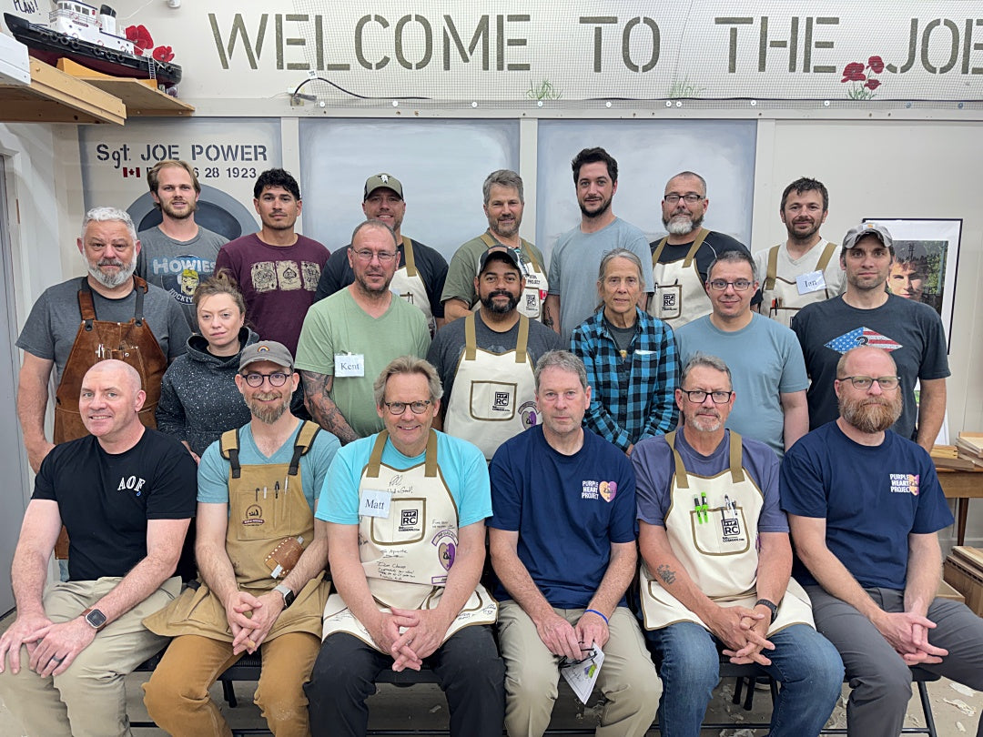 Group of people wearing aprons and casual clothing in a workshop setting with 'Welcome to The Joe' sign.